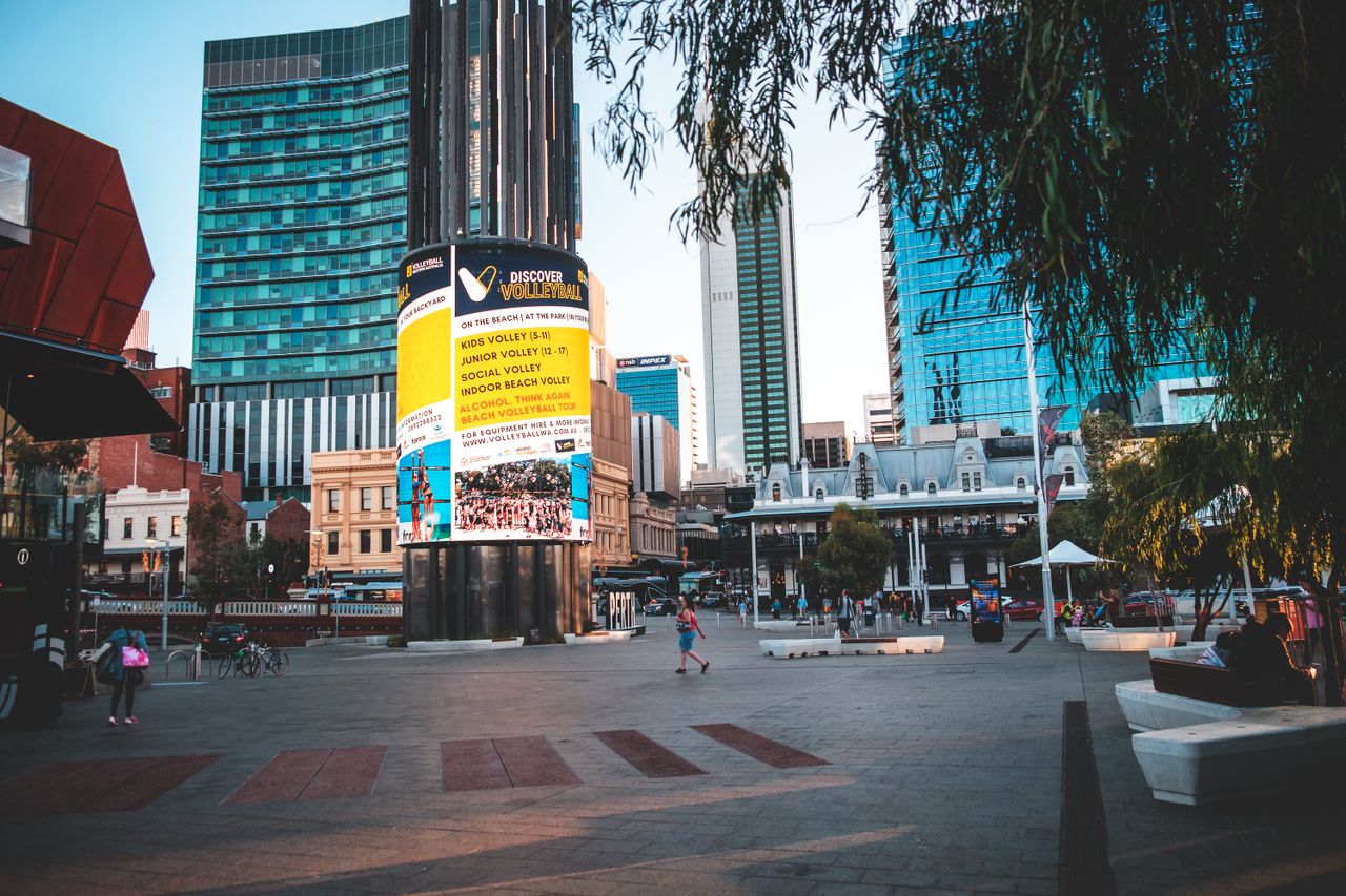 People walking in square with tall glass buildings and modern round shaped signboard in city